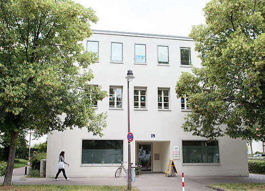 Das Bild zeigt die Vorderansicht des Hauses an der Esplanade 1. Das Haus ist weiß gestrichen, es hat viele Fenster, links und rechts wird es umrahmt von zwei Bäumen.